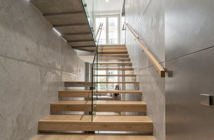 Vue d'ensemble d'une cage d'escalier moderne rénovée avec des matériaux mixtes bois, verre et béton dans un appartement parisien